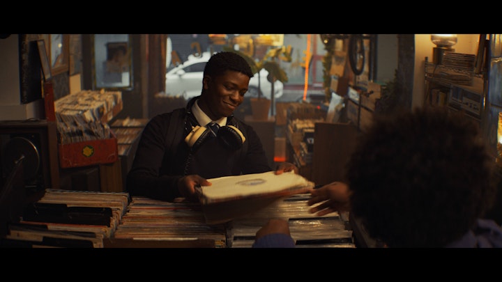 Still from 1 UP, the lead handing a record across the counter of a record shop