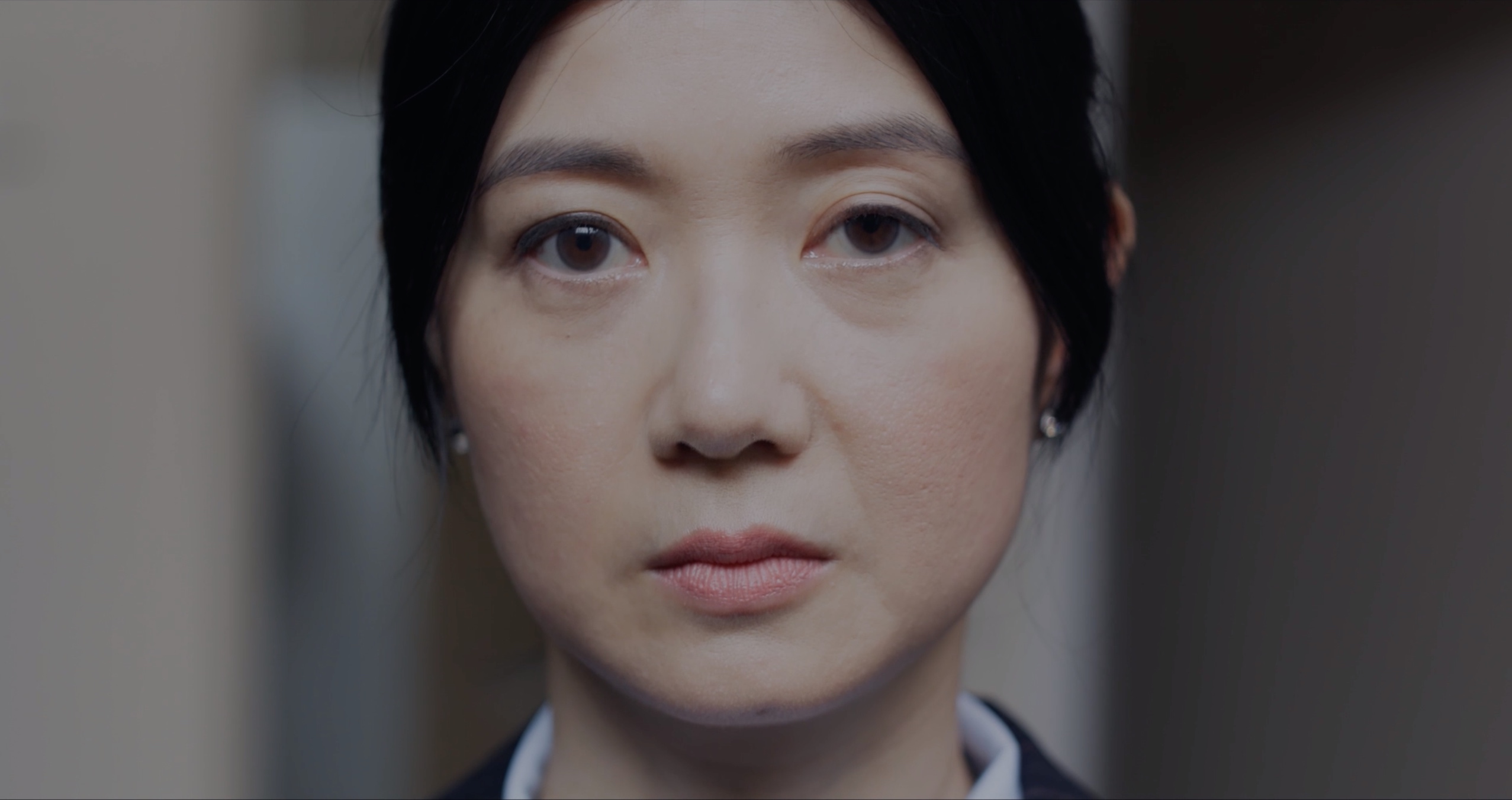Still from British People, a close portrait of Mei looking off camera in a pale corridor
