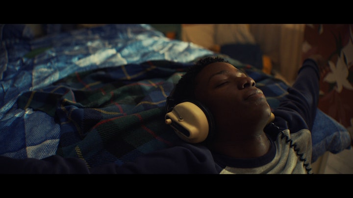 Still from 1 UP, the lead lying on his bed with his eyes closed, listening