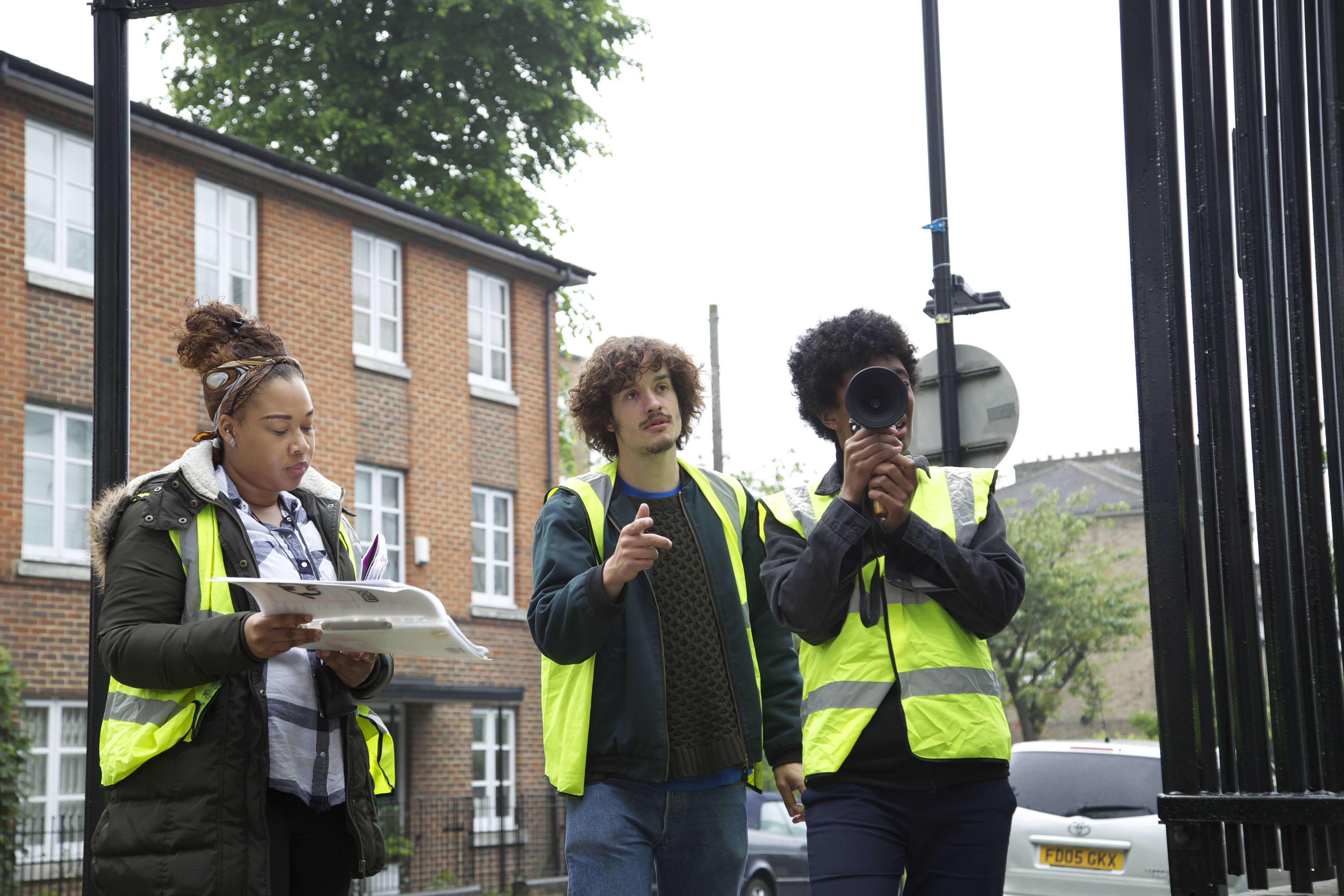Behind the scenes on We Love Moses, crew in high visibility jackets filming outside a housing block