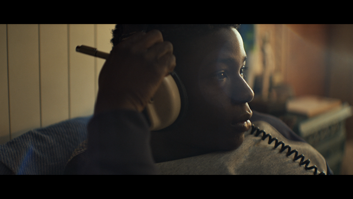 Still from 1 UP, the lead adjusting his headphones in a warmly lit bedroom