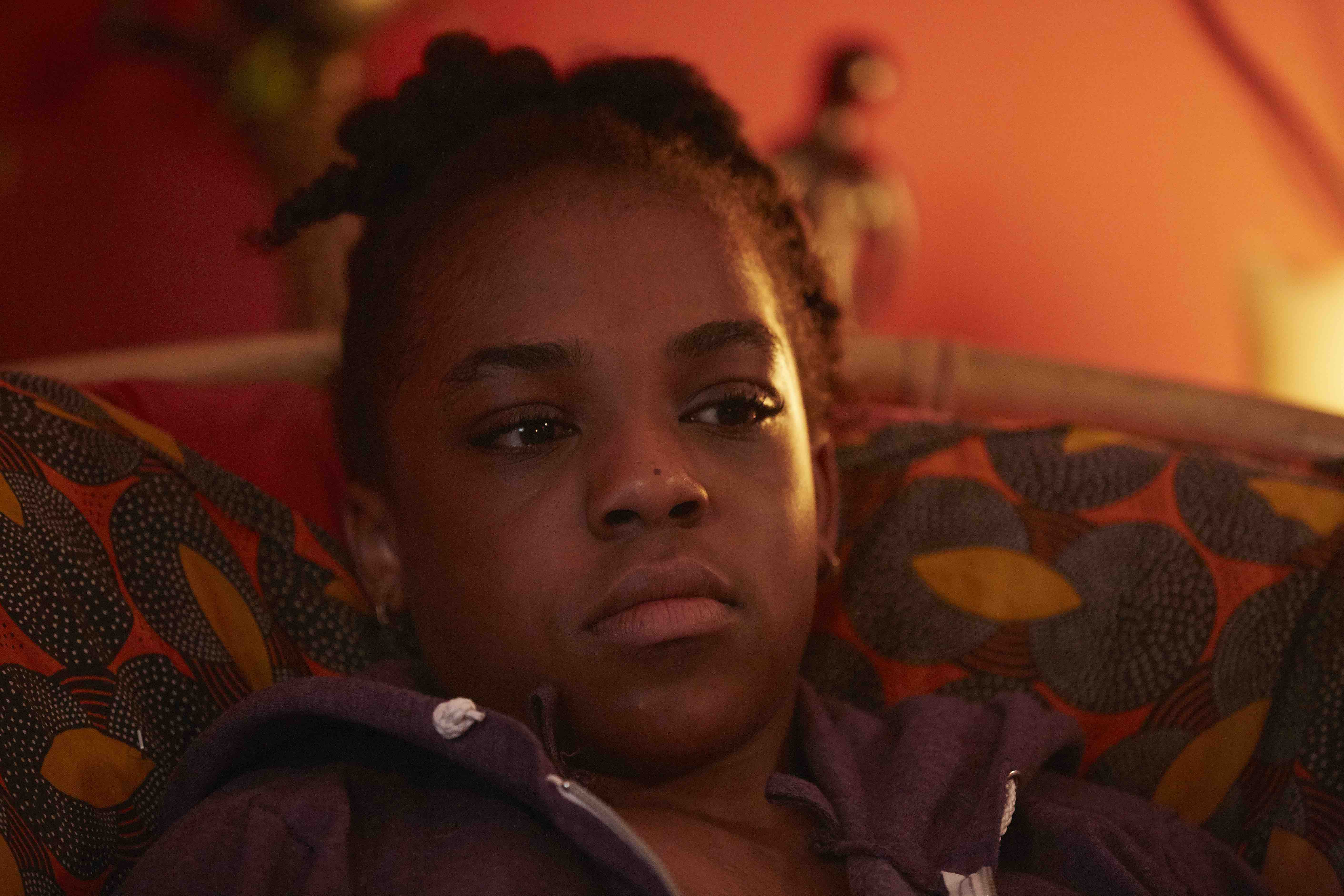 Still from We Love Moses, Ella lying on a bed in a warm orange room