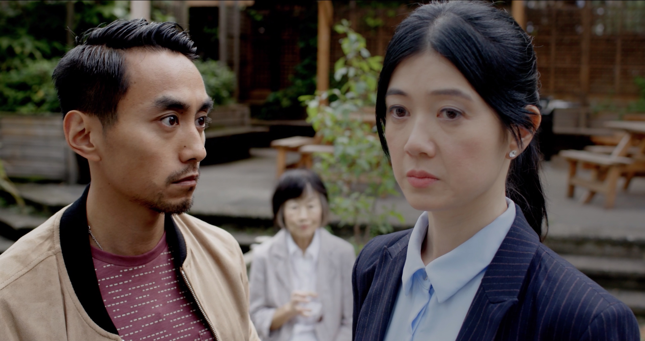 Still from British People, two characters standing together in a garden courtyard