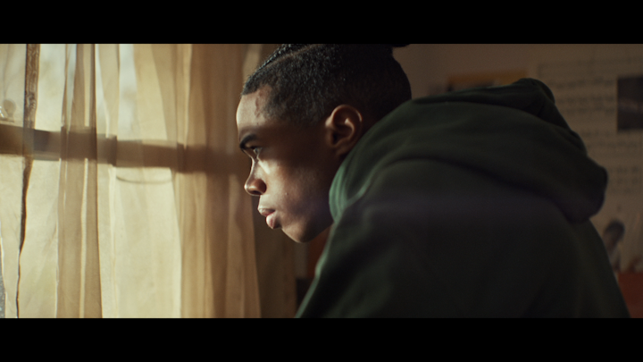 Still from 1 UP, a young man in a hooded top looking out of a window